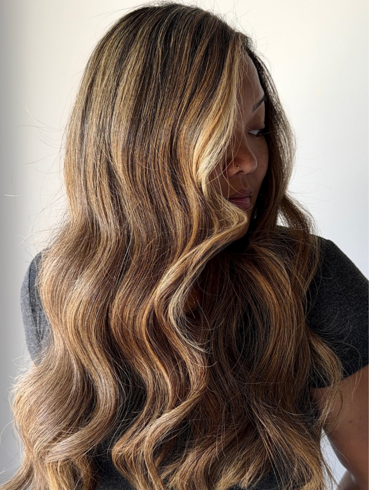 Woman with long brunette hair with honey blonde highlights in front of a white background